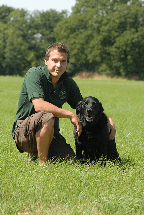 A Hunter's Lodge employee sat on the grass with a black Labrador.
